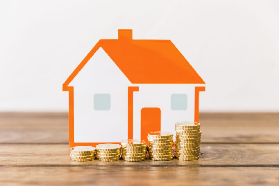 close-up-increasing-stacked-coins-house-model-wooden-desk