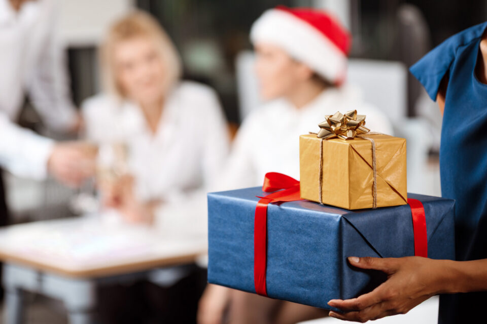 Happy cheerful colleagues celebrating christmas party in office smiling giving presents. Focus on gift box.