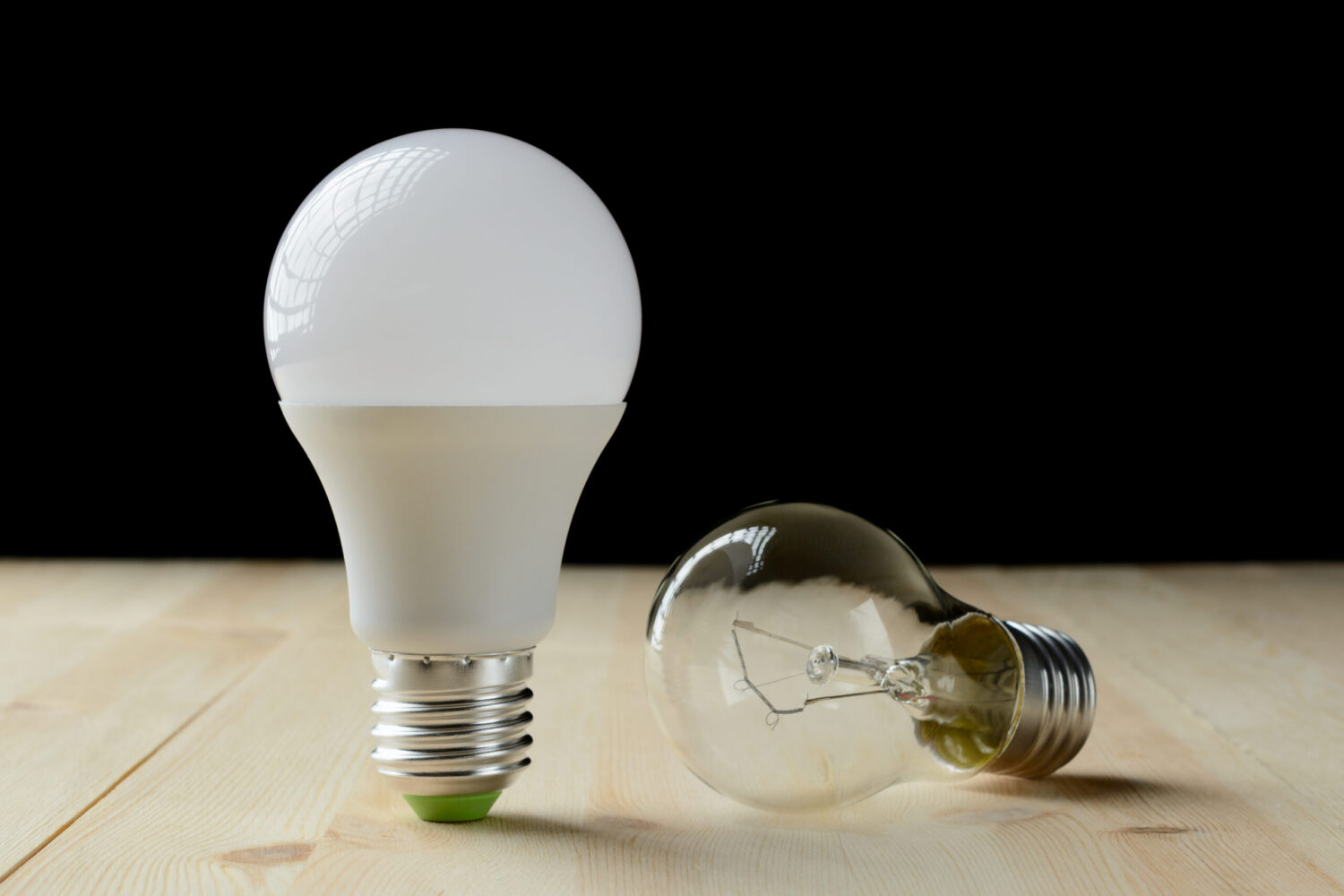 LED lamp standing on a wooden table, near an incandescent lamp lie