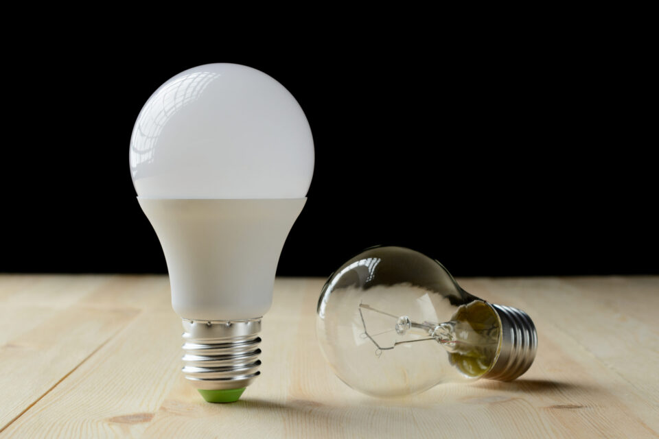 LED lamp standing on a wooden table, near an incandescent lamp lie
