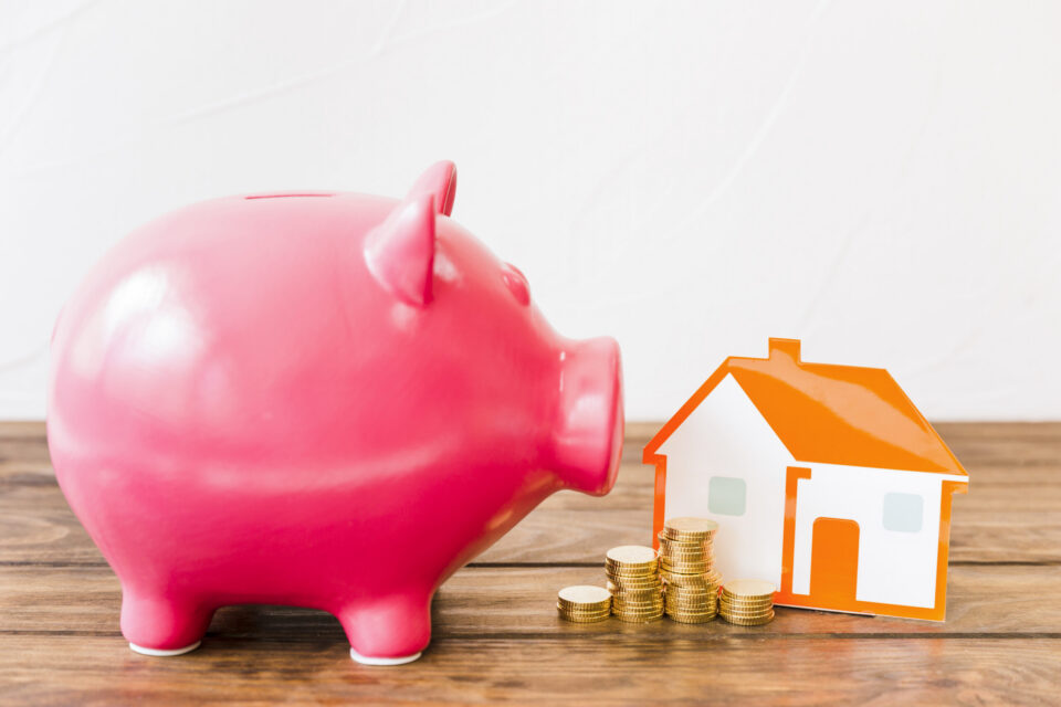 pink-piggybank-near-stacked-coins-house-wooden-desk